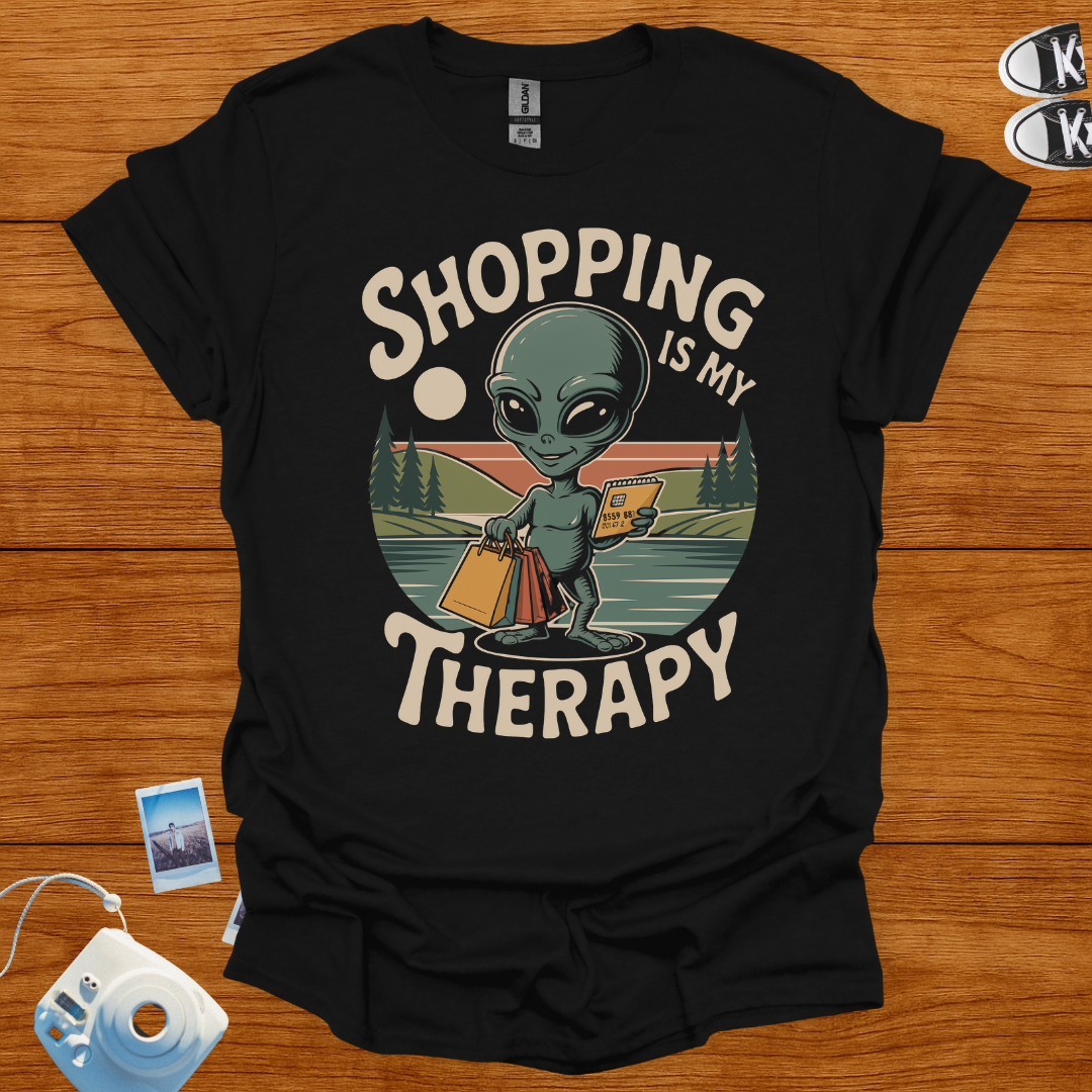 Black t-shirt with alien graphic and 'Shopping is my Therapy' text on a wooden surface.