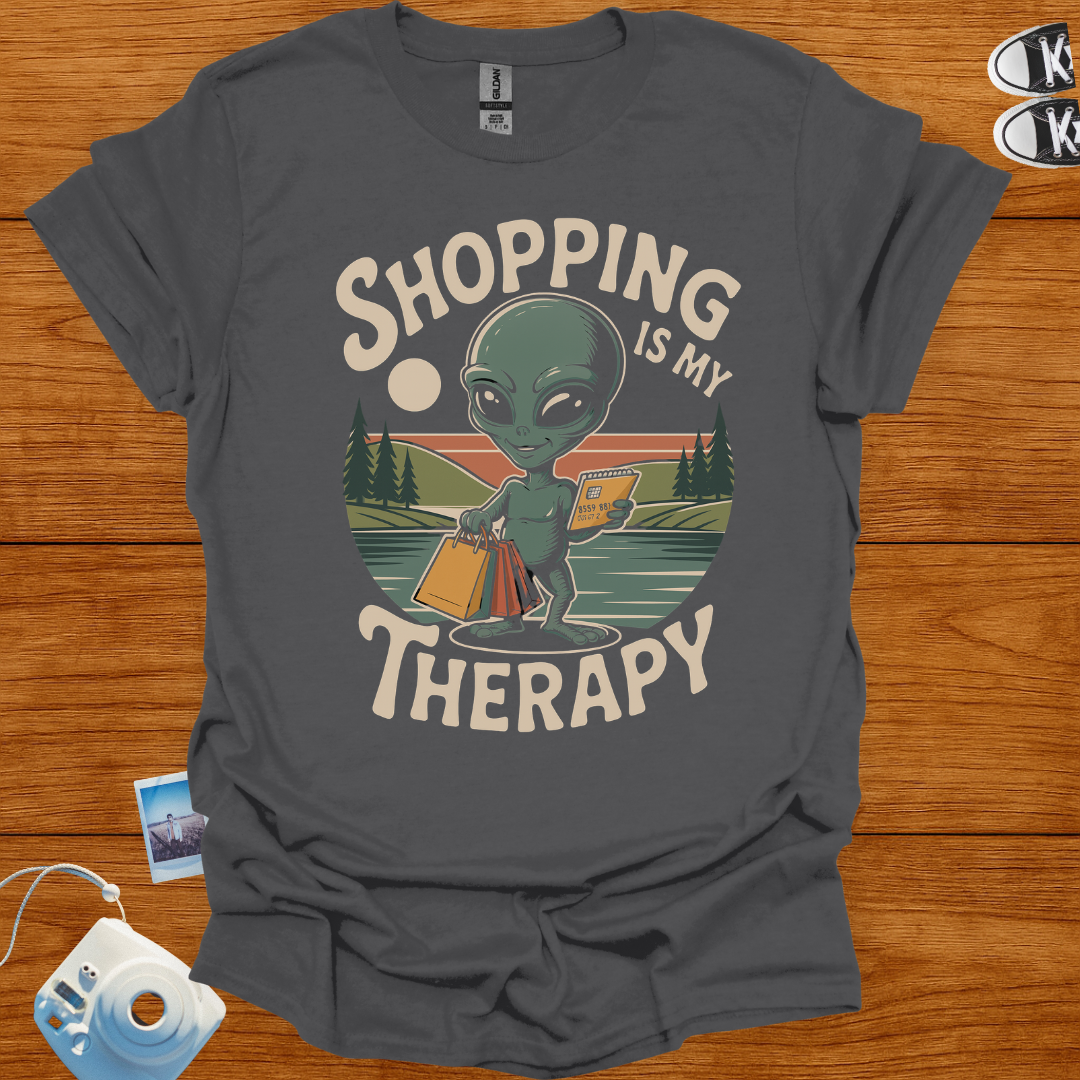 Gray t-shirt with alien graphic and 'Shopping is my Therapy' text on a wooden surface.